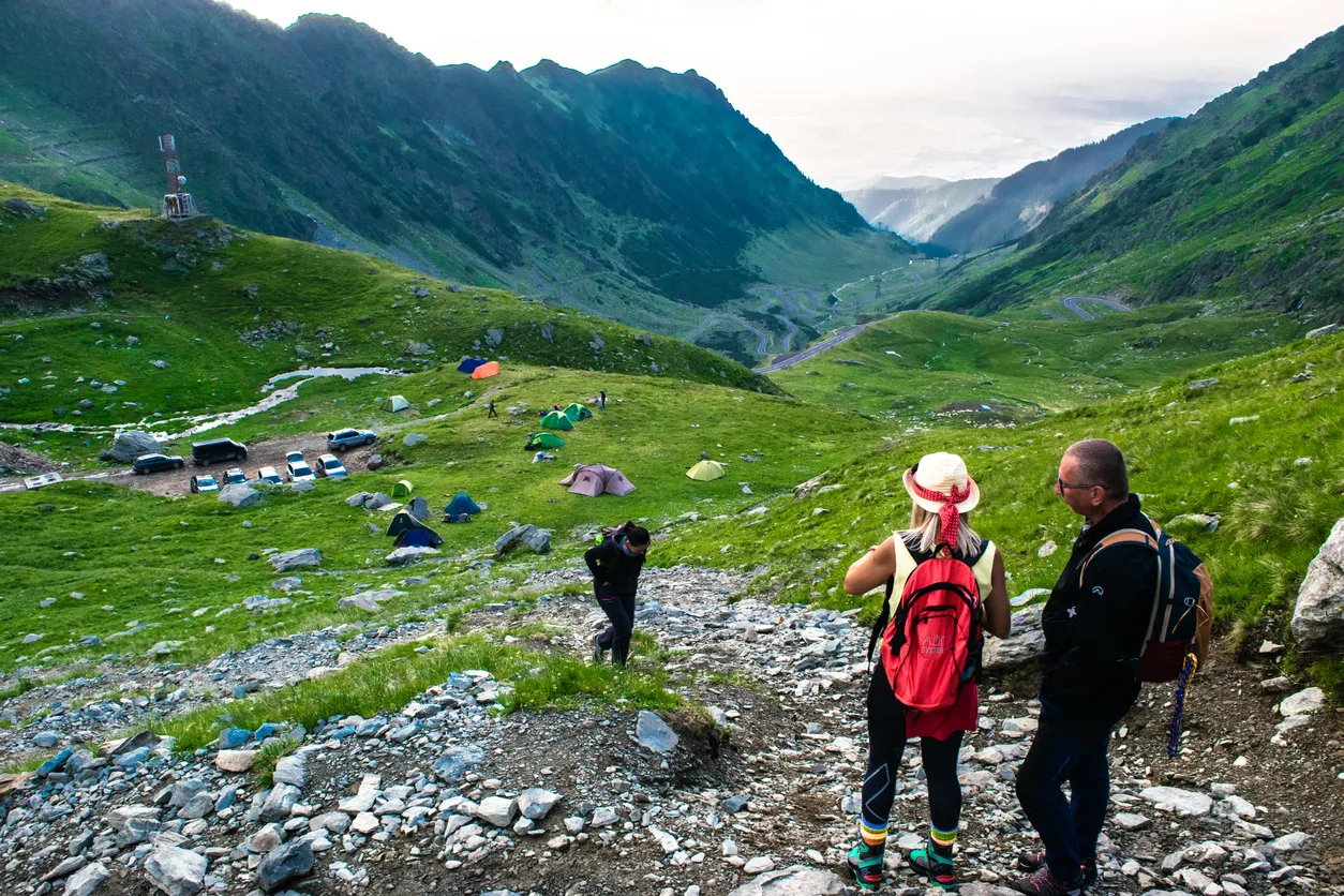 Transfagarasan road, Romania - June 23, 202: Tourists on mountain path near pass of popular tourist Transfagarasan road, one of most beautiful roads in world. Top view of tourists tents and road bends