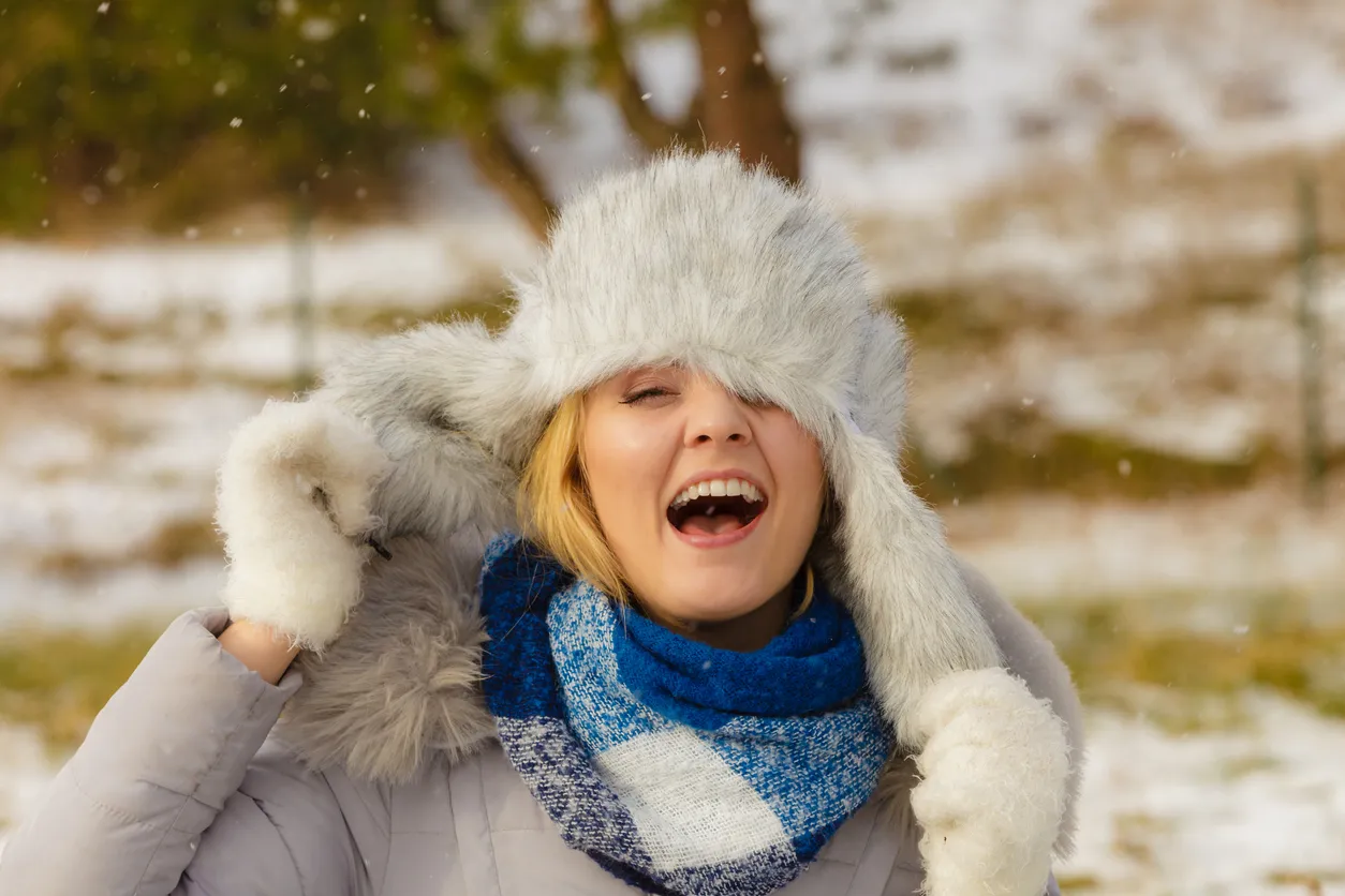 Pretty young woman wearing warm accessories during winter time. Female having grey warm hat made of light fur and blue scarf.