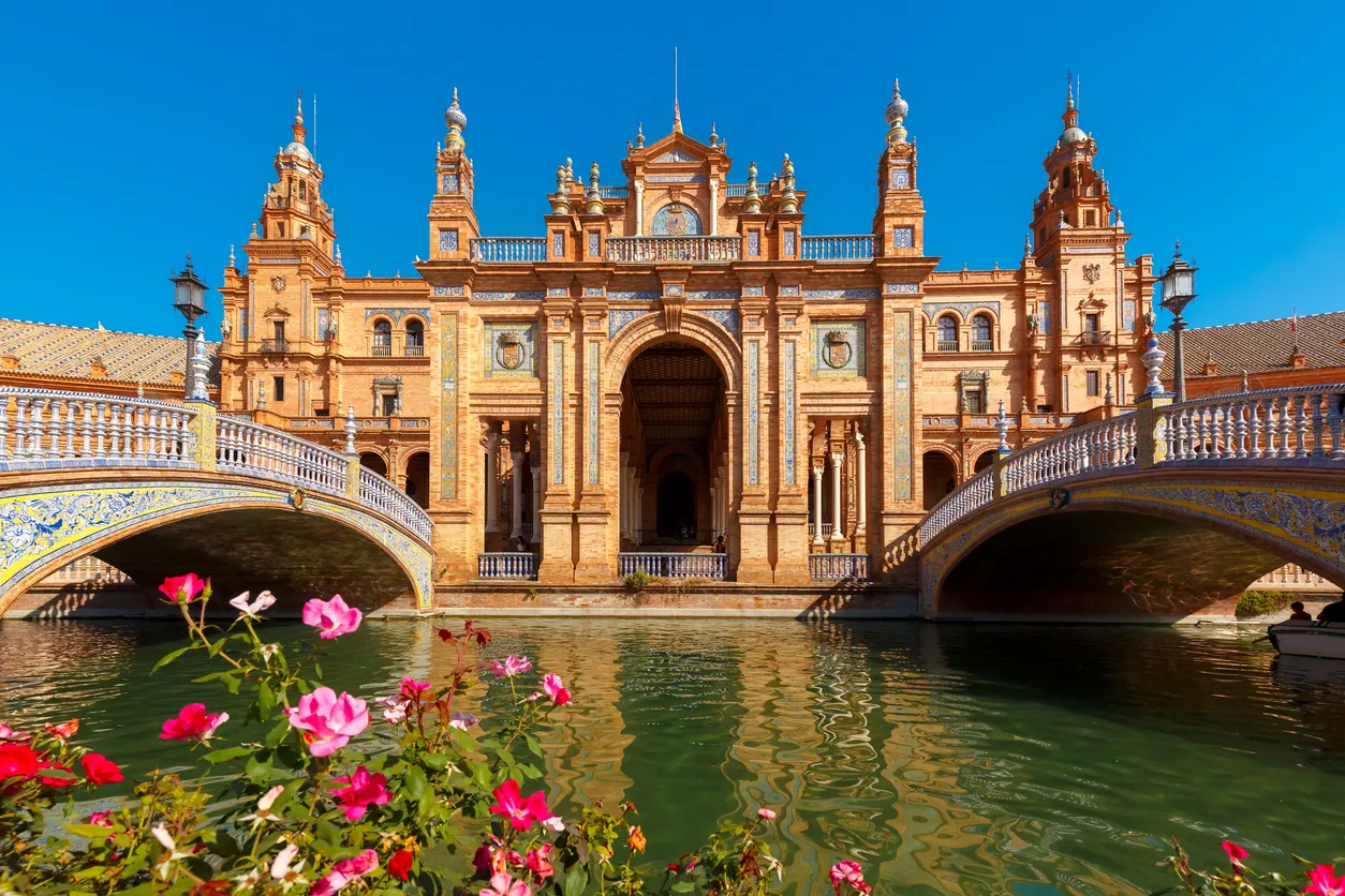 Spain Square or Plaza de Espana in Seville in the sunny summer day, Andalusia, Spain. Flower beds, bridges and channel in the foreground