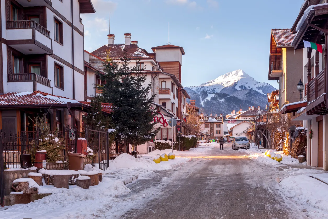Bansko, Bulgaria - January 28, 2021: Street view, traditional houses and Todorka snow mountain peak in bulgarian ski resort