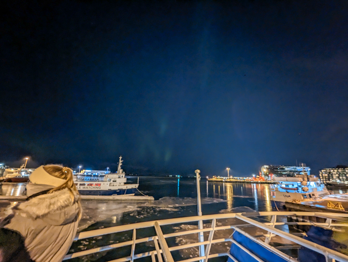 Boat starting to make its way out of Reykjavik harbour with flashes of green on the horizon of the darkening sky. 
