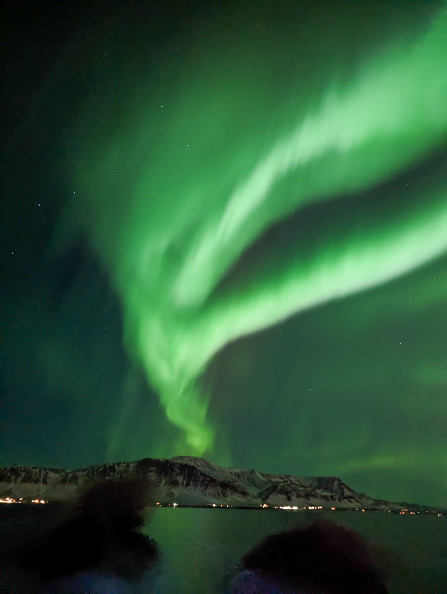 View of the Northern Lights from a boat close to Reykjavik harbour with the mountains in the distance. 