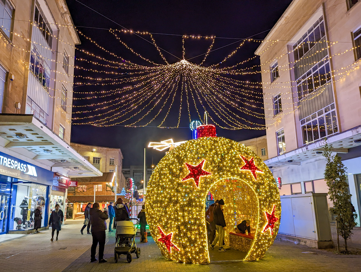 Bright glittery bauble with lights around it and lights strung above at a English Christmas market